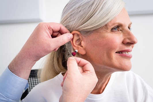 Eine ältere Frau bekommt ein modernes Hörgerät angepasst und lächelt zufrieden.